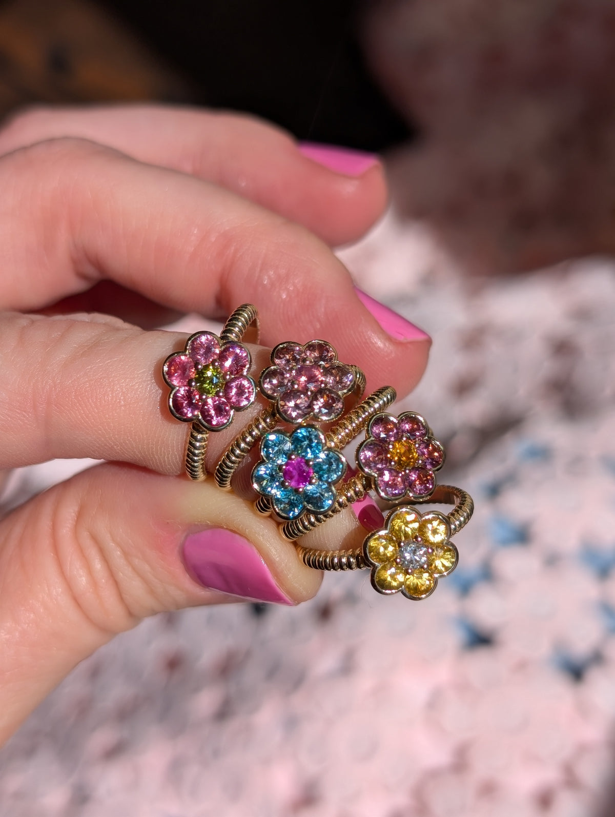 Five Blooms Medium Rings held between the fingers, close-up of the stones and twisted gold bands
