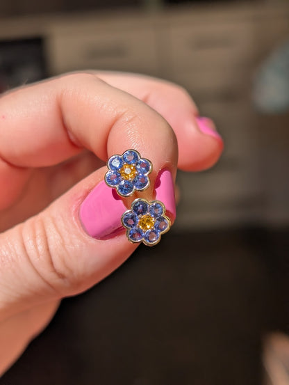 Blooms Stud Earrings in tanzanite with spessartite garnet center, close-up held in hand