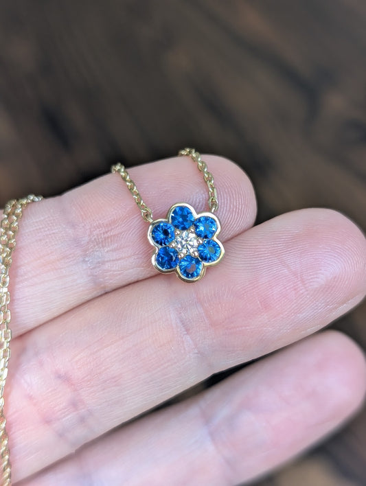 Small Blooms Pendant in blue sapphire with diamond center, close-up on fingers