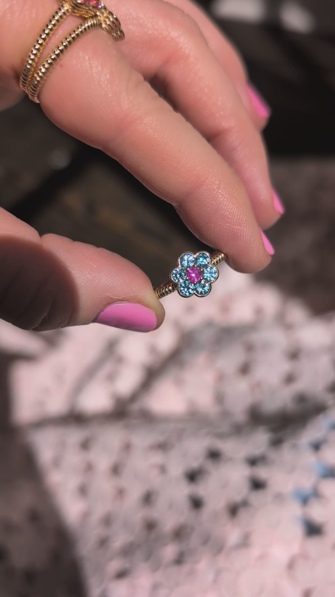 Video of the Blooms Medium Ring in blue zircon and pink ruby held in sunlight
